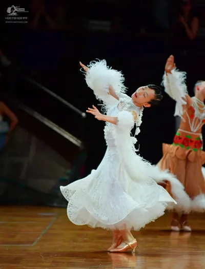Dancesport competitor: Female dancer in foreground: white ballroom dress featuring lace, a voluminous s
