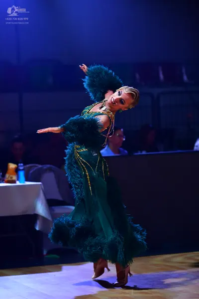 Dancesport competitor: Female dancer: emerald green ballroom gown featuring large feathery or fringed s