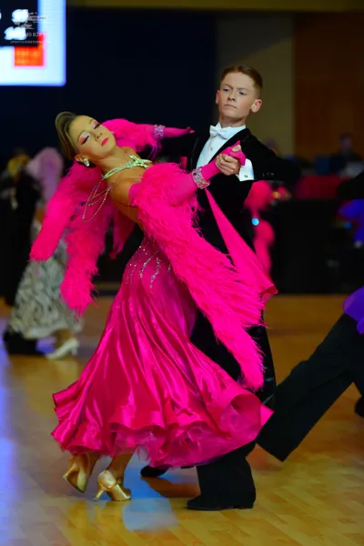 Dancesport competitor: Female dancer: bright pink ballroom dress with a large pink feather boa accent a