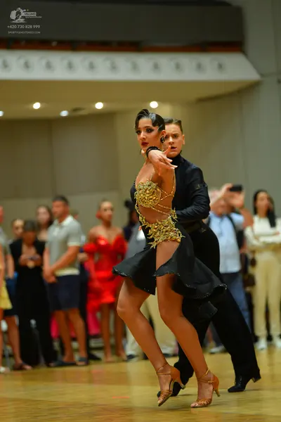 Dancesport competitor: Female dancer: black Latin dance dress with gold sequin embellishments on the bo