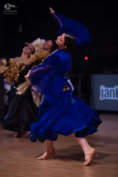 Dancesport competitor: Female dancer in foreground: royal blue ballroom gown with large, flowing, sheer