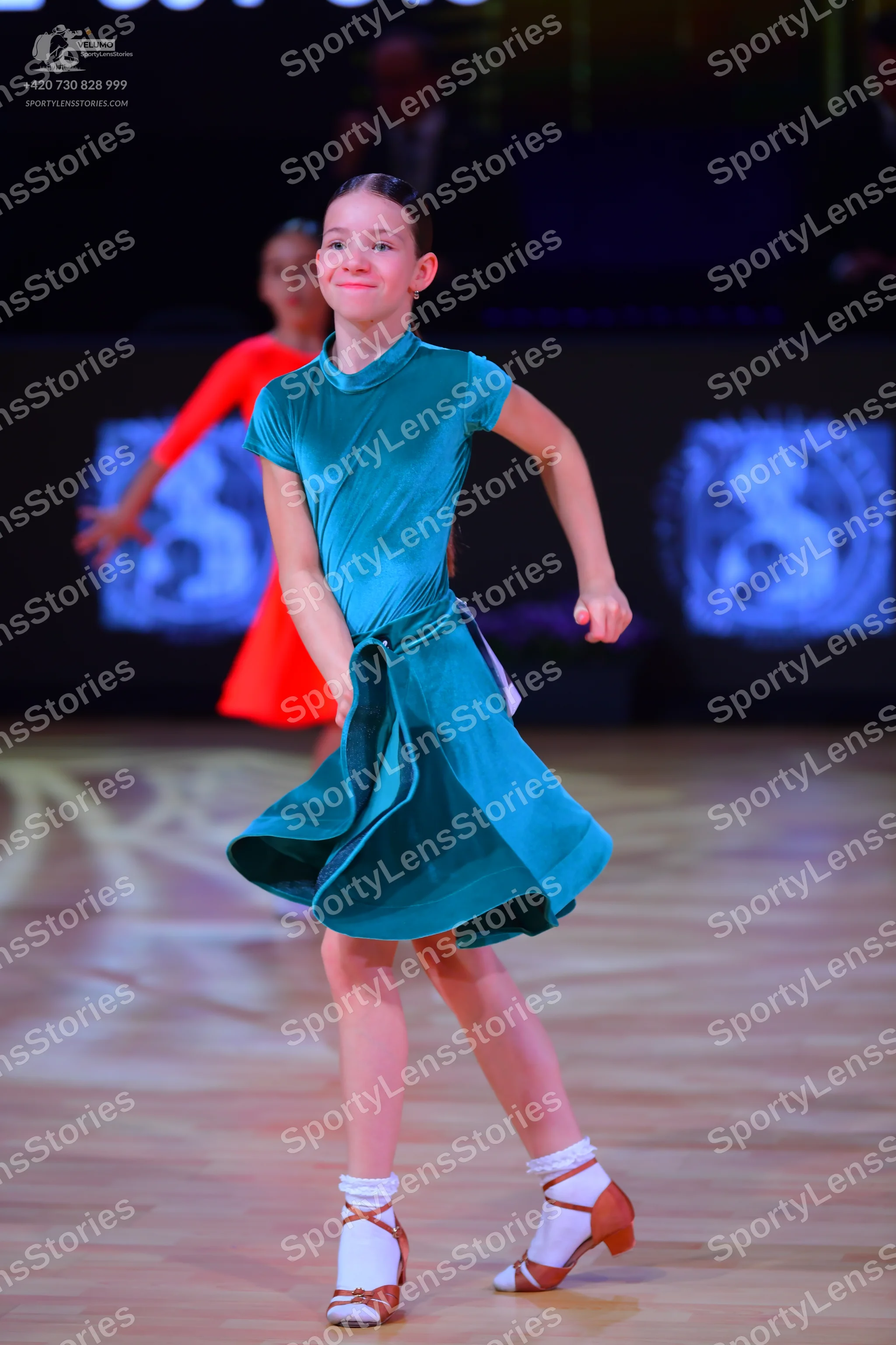 Dancesport competitor: Female dancer in foreground: teal satin Latin dress with a high neck and flared 