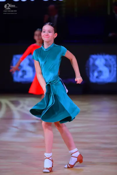 Dancesport competitor: Female dancer in foreground: teal satin Latin dress with a high neck and flared 