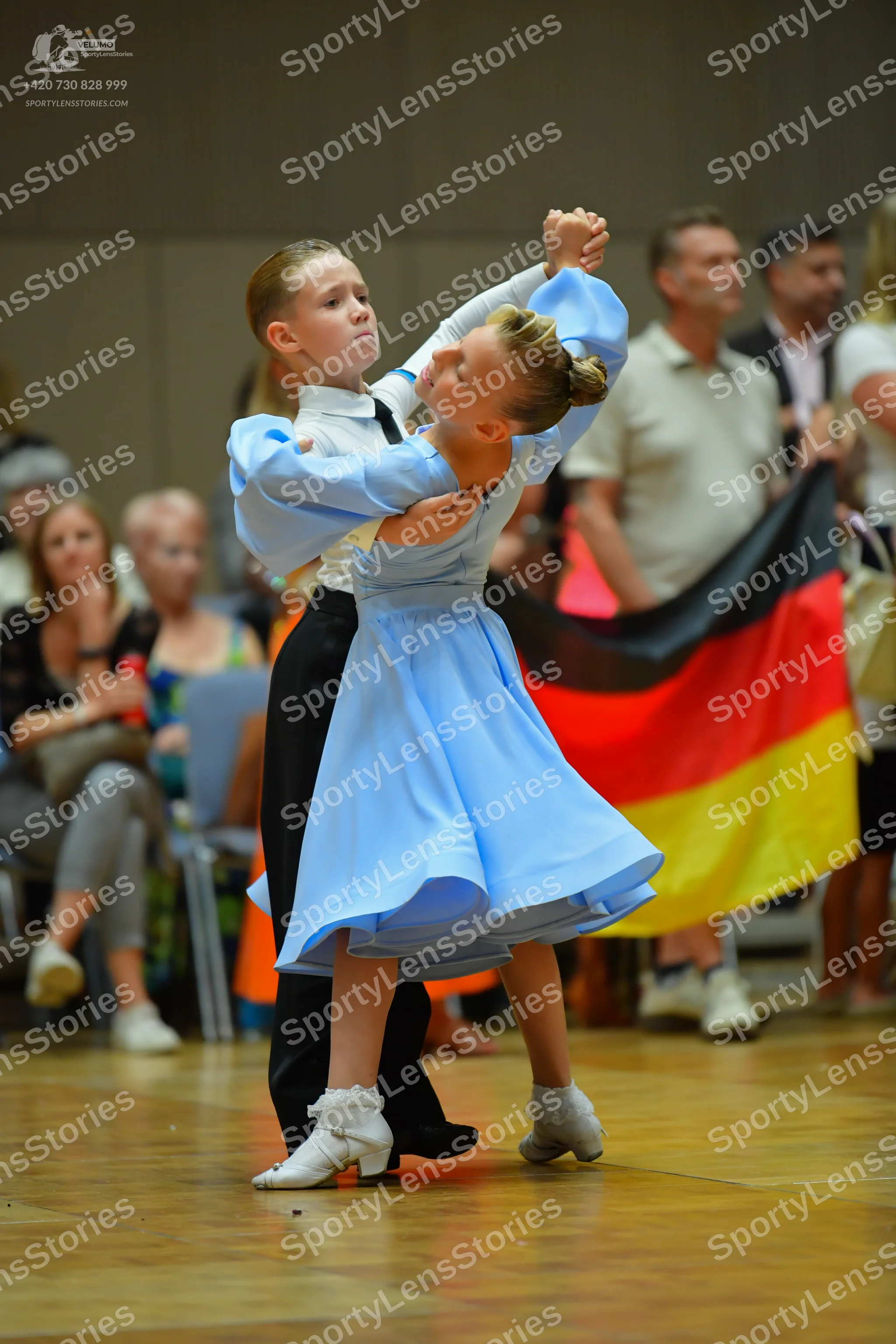 Dancesport competitor: Female dancer: light blue long-sleeved dress with a flared skirt, appearing to b