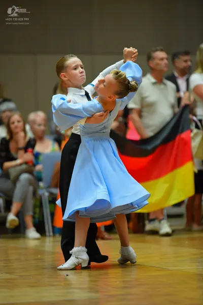 Dancesport competitor: Female dancer: light blue long-sleeved dress with a flared skirt, appearing to b
