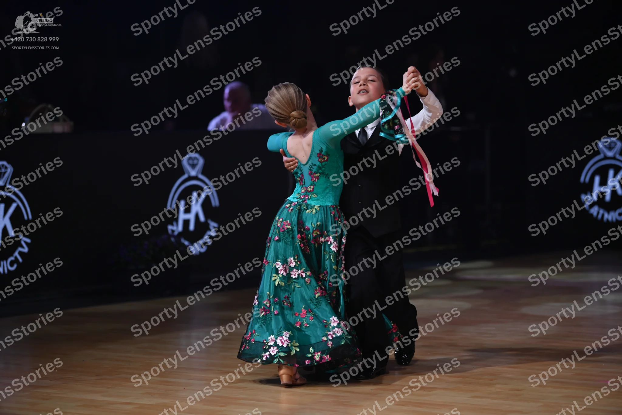 Dancesport competitor: Female dancer: teal long-sleeved ballgown with a floral pattern on the skirt