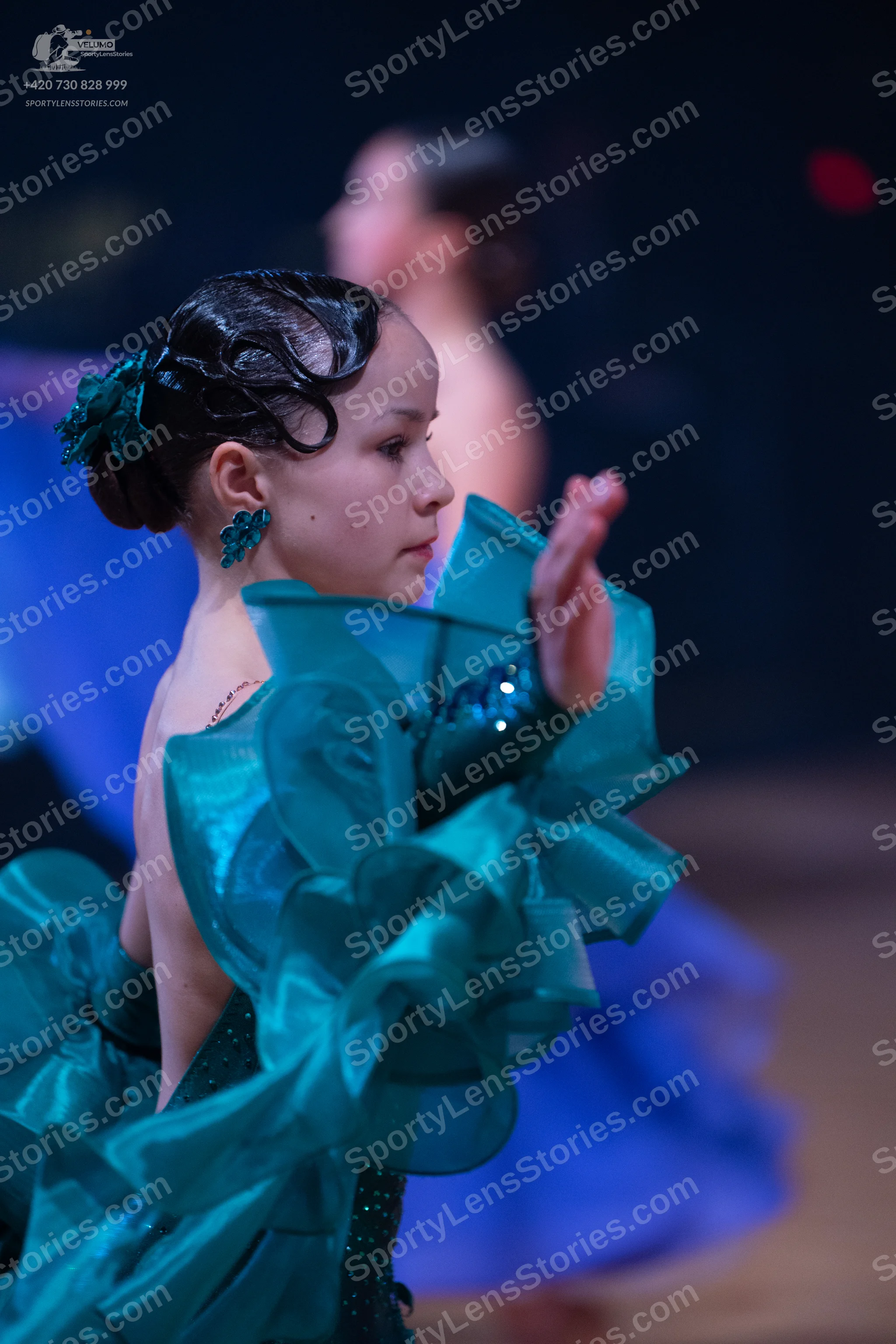 Dancesport competitor: Female dancer in foreground: teal ballgown with large, voluminous satin-like ruf