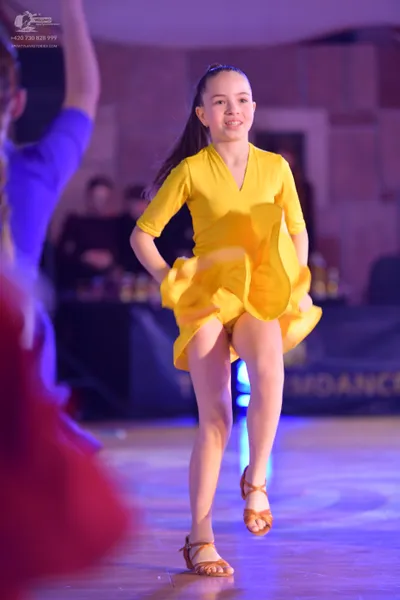 Dancesport competitor: Female dancer in center: yellow Latin dress with three-quarter length sleeves an
