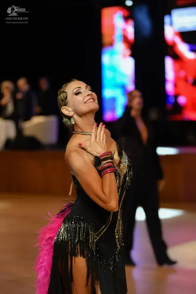 Dancesport competitor: Female dancer: black latin dress with gold fringe and pink feathers