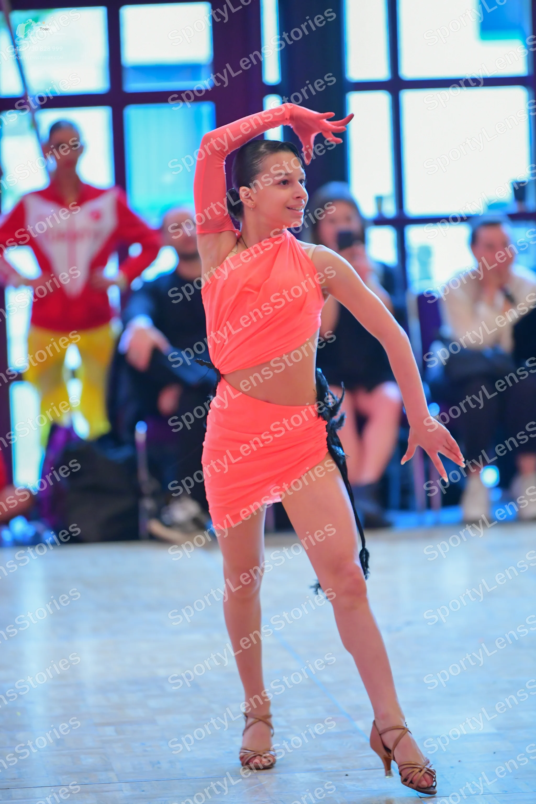 Dancesport competitor: Female dancer (foreground): coral-colored two-piece Latin dance costume featurin