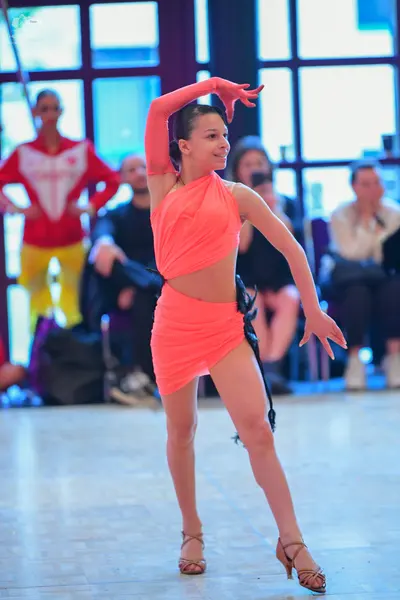 Dancesport competitor: Female dancer (foreground): coral-colored two-piece Latin dance costume featurin