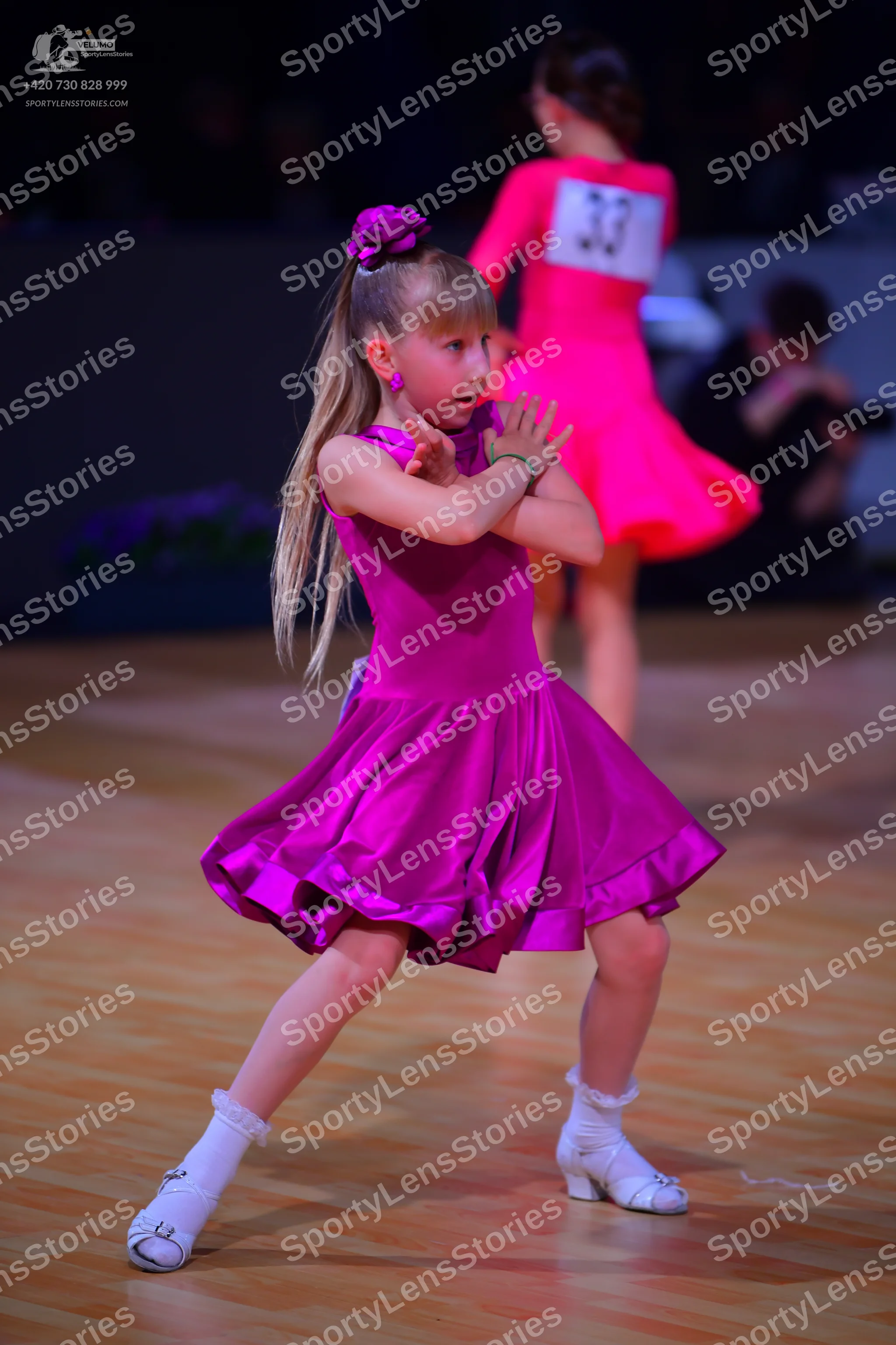 Dancesport competitor: Female dancer in foreground: magenta satin sleeveless dress with a flared skirt,