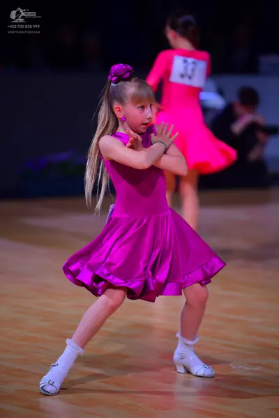 Dancesport competitor: Female dancer in foreground: magenta satin sleeveless dress with a flared skirt,