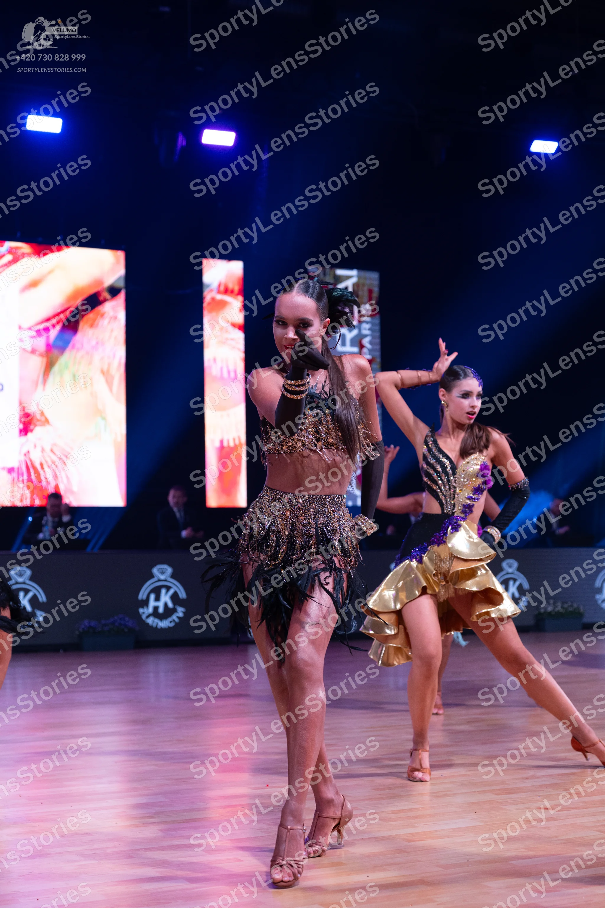Dancesport competitor: Female dancer in foreground: bronze-colored two-piece Latin costume with heavy s