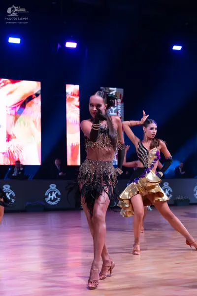 Dancesport competitor: Female dancer in foreground: bronze-colored two-piece Latin costume with heavy s