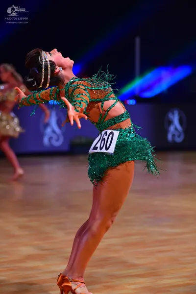 Dancesport competitor: Female dancer in foreground: emerald green sequin latin dress with cut-out detai
