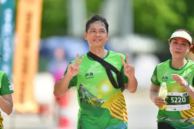 Marathon runner #5220: Runner 1: green jersey with yellow pattern, black strap across chest, blue short