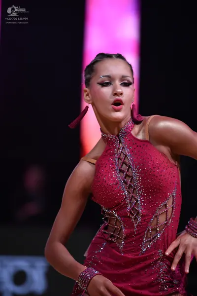 Dancesport competitor: Female dancer: dark pink Latin dance dress covered in crystals, featuring a halt