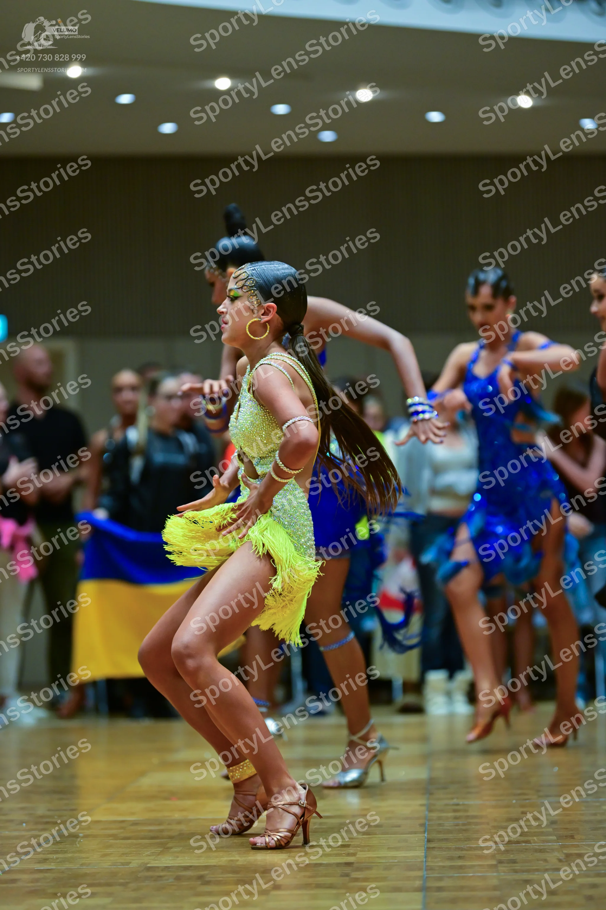 Dancesport competitor: Female dancer in foreground: yellow latin dress with sequins and fringe, accesso