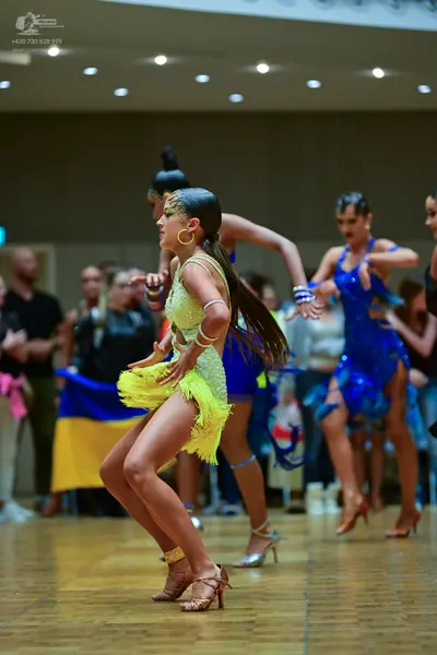 Dancesport competitor: Female dancer in foreground: yellow latin dress with sequins and fringe, accesso