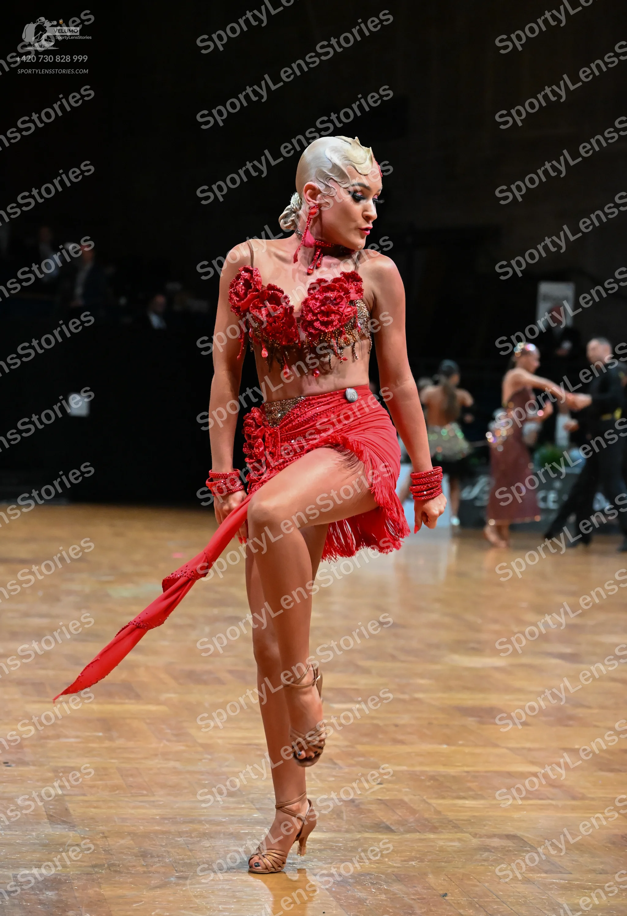 Dancesport competitor: Female dancer in foreground: red latin dress with rose appliqués on the bodice a