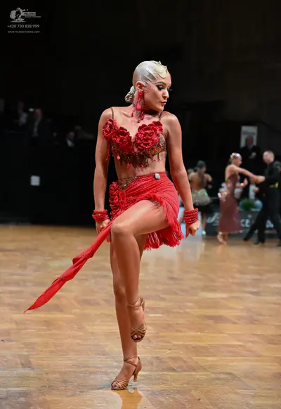 Dancesport competitor: Female dancer in foreground: red latin dress with rose appliqués on the bodice a