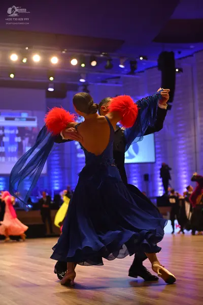 Dancesport competitor: Female dancer: royal blue ballroom gown with long, flowing sleeves and large red