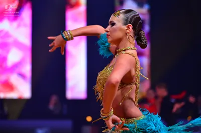 Dancesport competitor: Female dancer: teal Latin costume decorated with gold sequins and crystals, feat