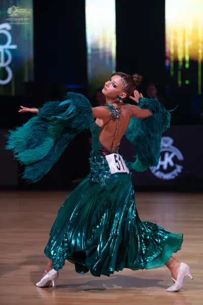Dancesport competitor: Female dancer: teal metallic ballgown with large feather sleeves and sparkly det