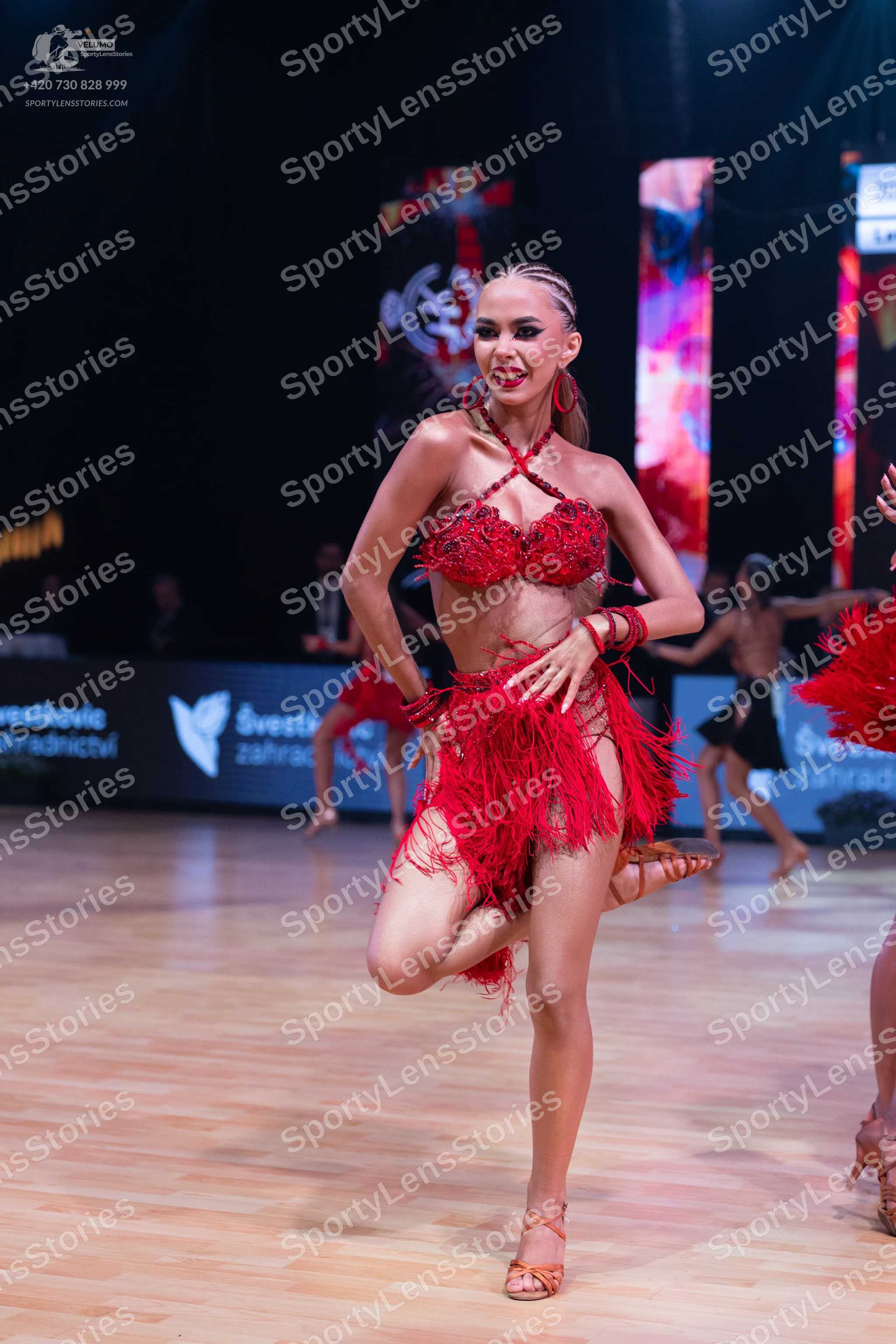 Dancesport competitor: Female dancer in foreground: red Latin dance costume consisting of a halter-neck