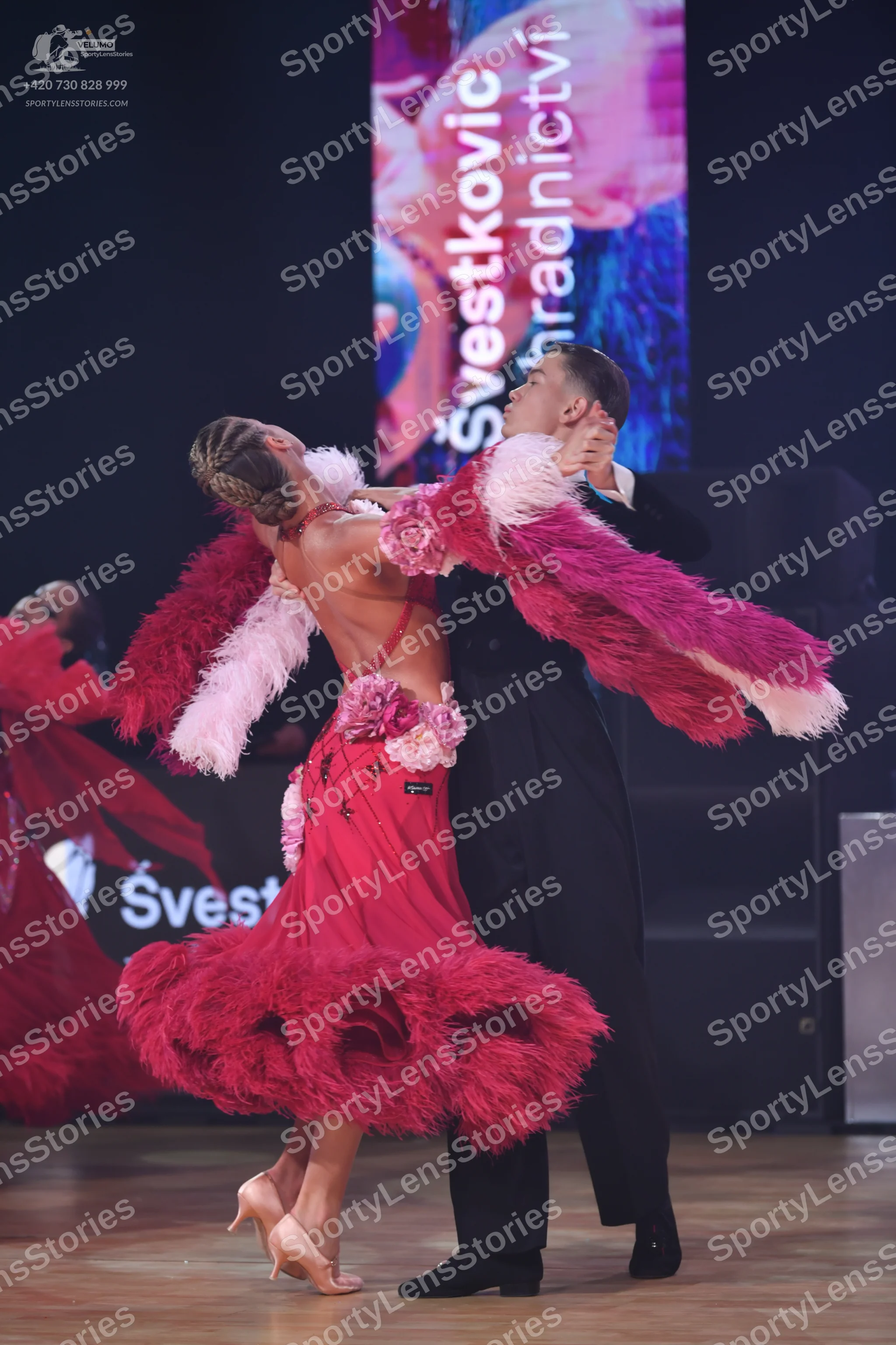 Dancesport competitor: Female dancer: red Latin dance dress with voluminous red, pink, and white feathe