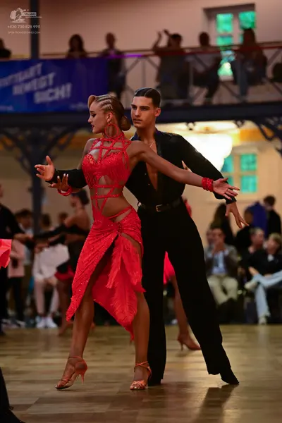 Dancesport competitor: Female dancer: red latin dress with intricate red lace/embellishments, featuring