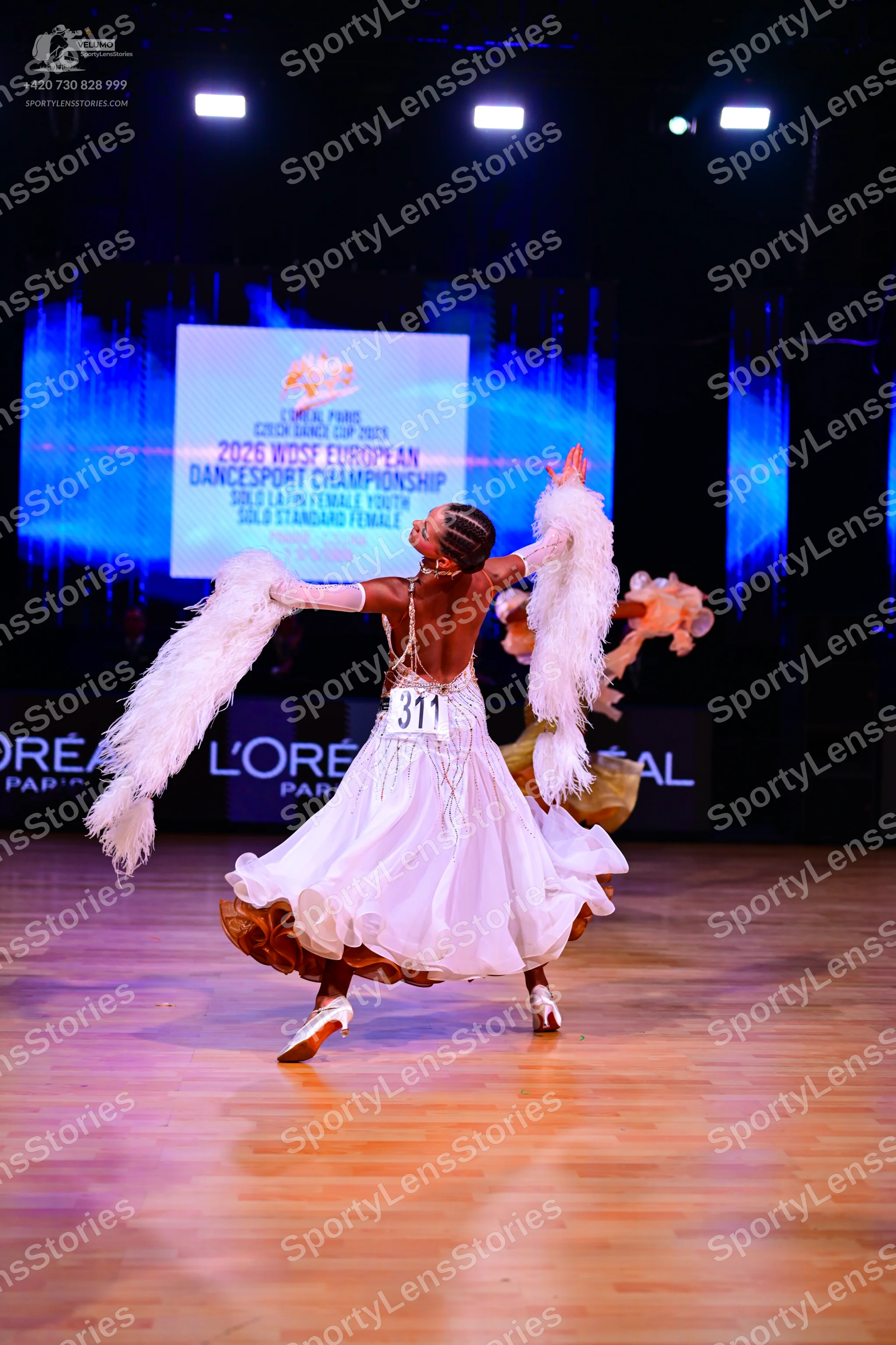 Dancesport competitor: Female dancer (foreground): white ballgown with large white feathered arm accent