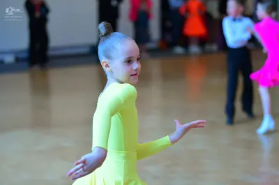 Dancesport competitor: Female dancer in foreground: bright yellow long-sleeved dance dress
