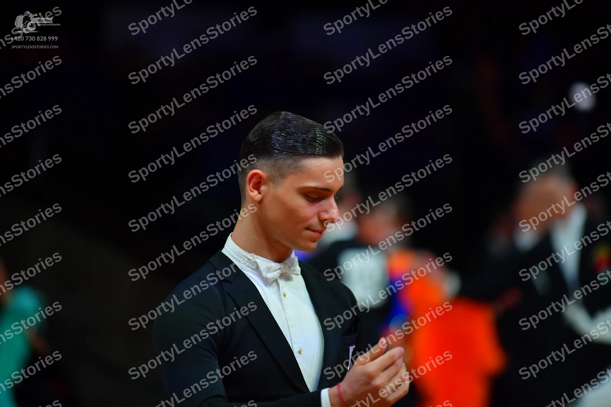 Dancesport competitor: Male dancer in foreground: black suit, white shirt, and white bow tie