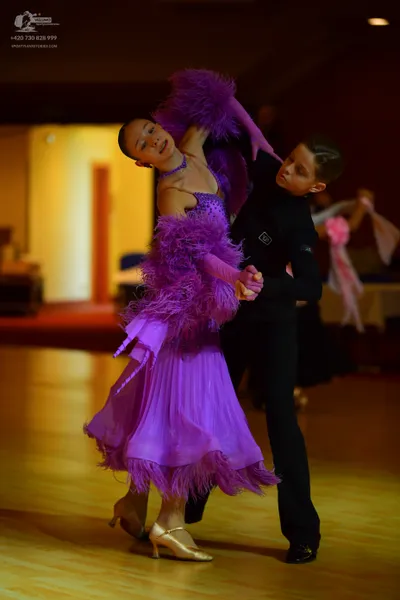 Dancesport competitor: Female dancer: purple Latin dress featuring large feather trim on the sleeves an