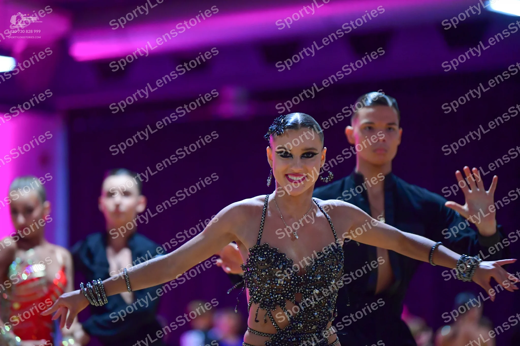 Dancesport competitor: Female dancer in foreground: dark grey/black Latin dance costume with heavy sequ