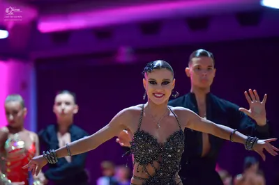 Dancesport competitor: Female dancer in foreground: dark grey/black Latin dance costume with heavy sequ