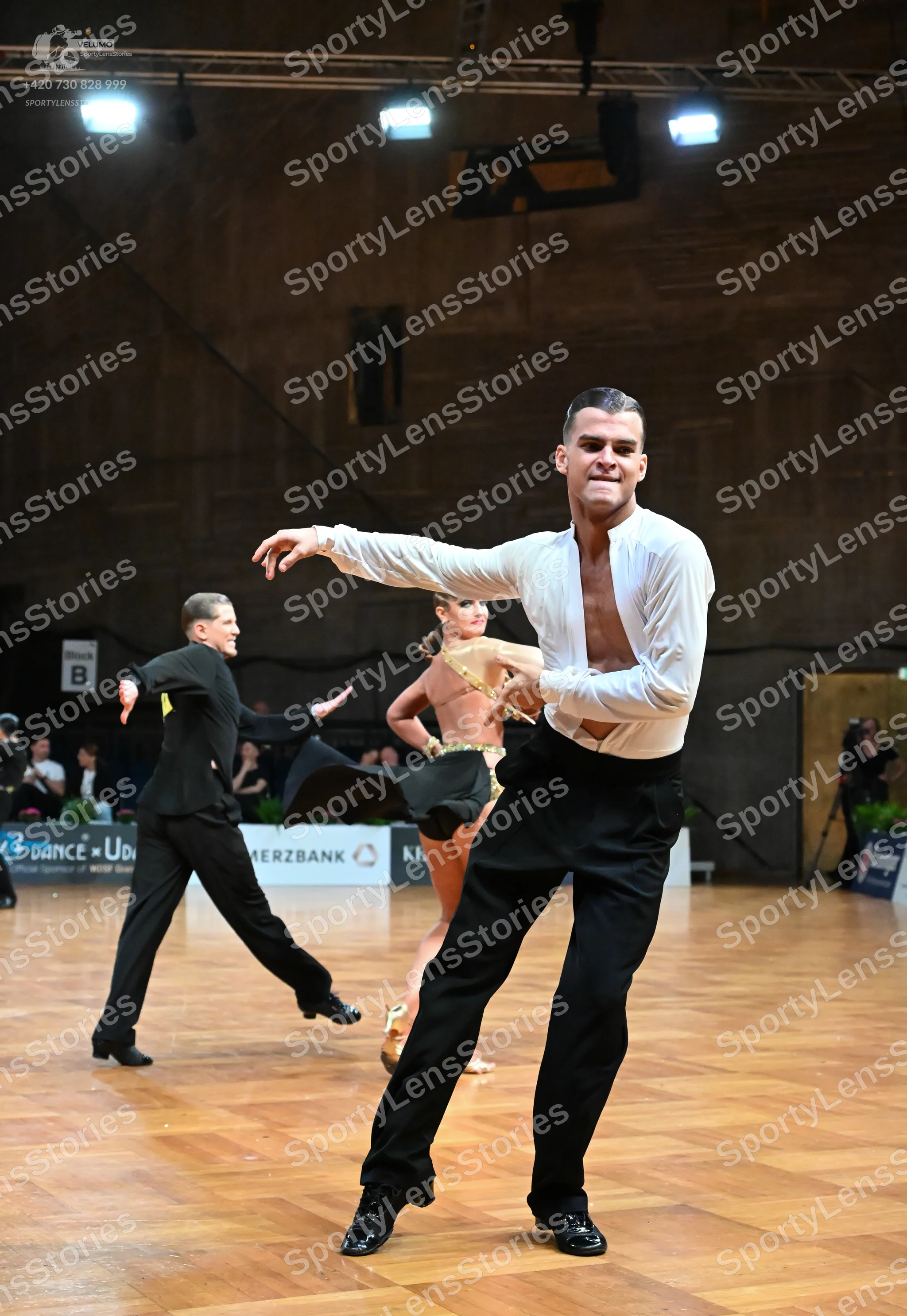 Dancesport competitor: Male dancer in foreground: white long-sleeved shirt and black trousers