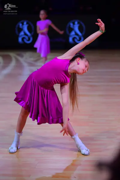 Dancesport competitor: Female dancer in foreground: magenta sleeveless dress with a flared, pleated ski