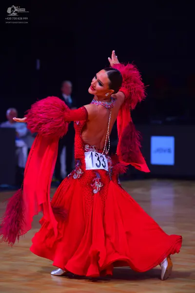 Dancesport competitor: Female dancer: red ballroom gown with large red feathered sleeves and crystal em