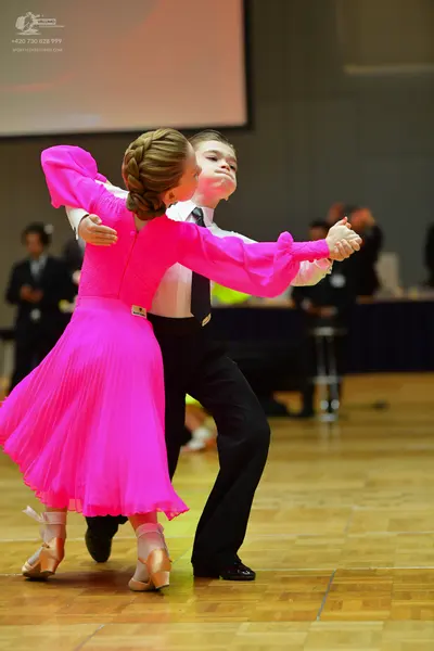 Dancesport competitor: Female dancer: bright pink long-sleeved ballroom dress with a pleated skirt and 