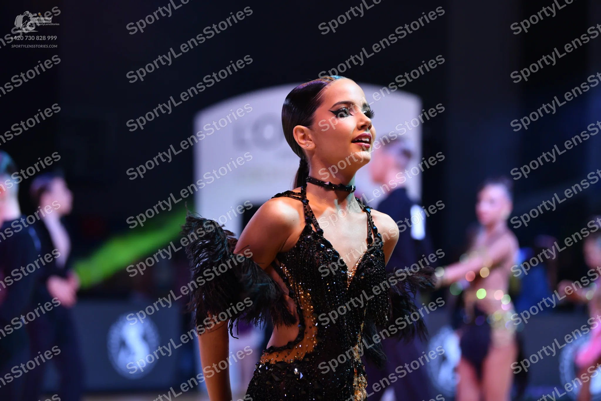 Dancesport competitor: Foreground female dancer: black latin dance dress with sequins and black feather