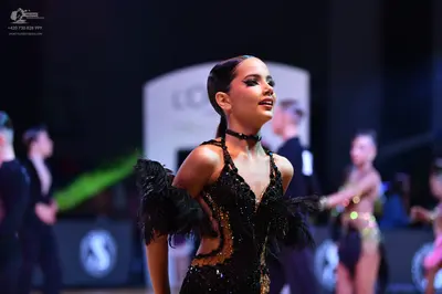Dancesport competitor: Foreground female dancer: black latin dance dress with sequins and black feather