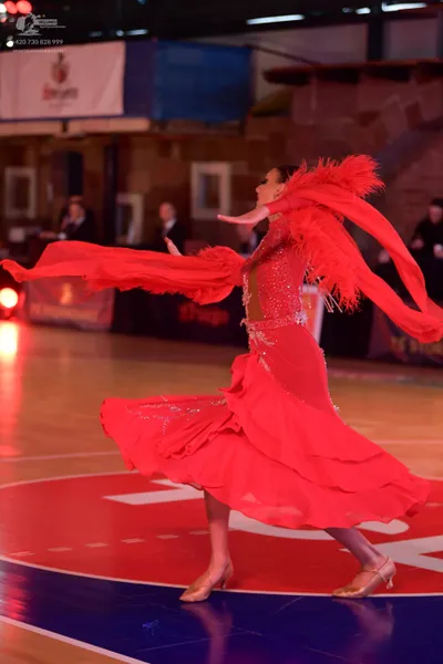 Dancesport competitor: Female dancer: bright red Latin dress with long, flowing sleeve extensions and s
