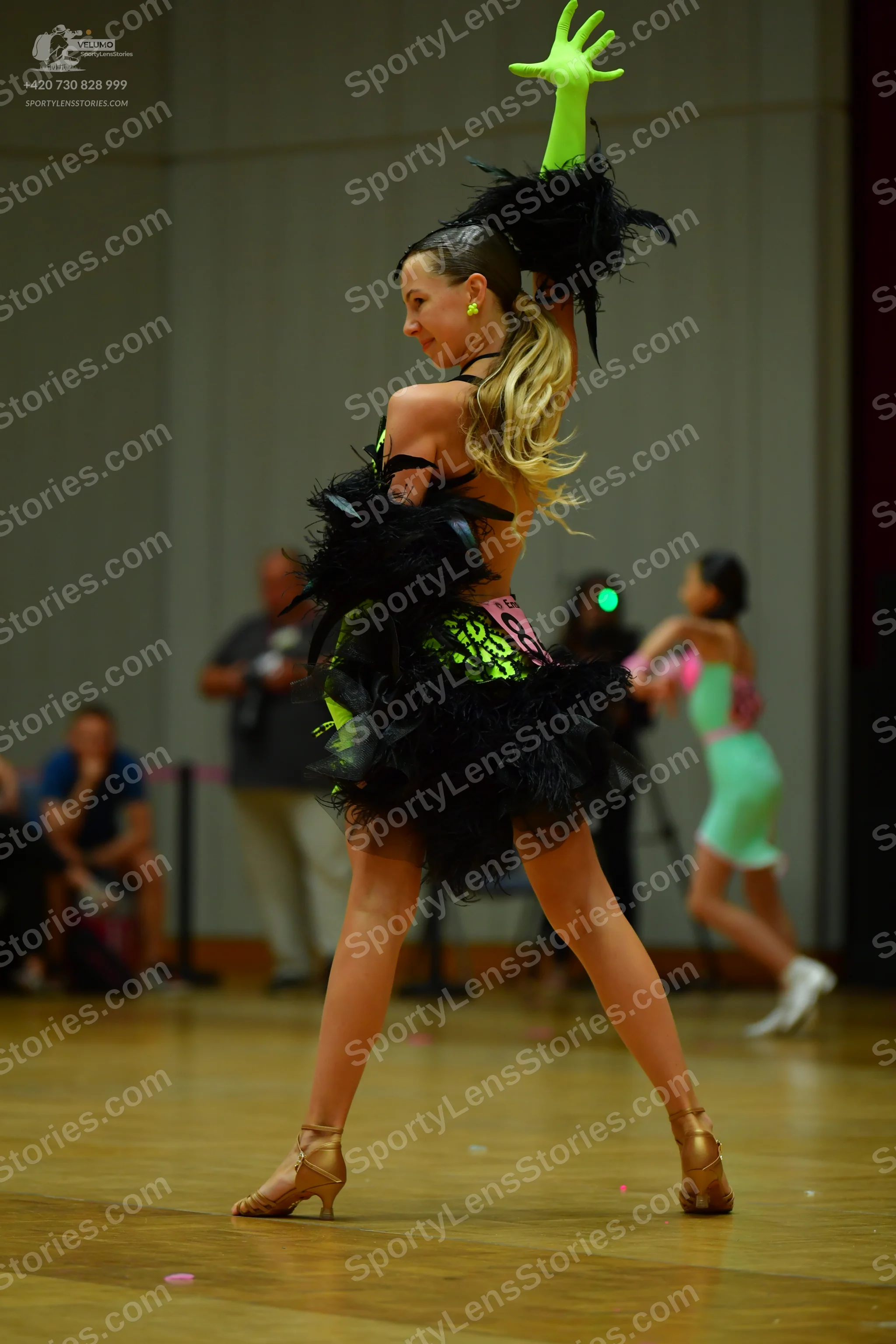 Dancesport competitor: Female dancer in foreground: black and neon green latin dress with large black f