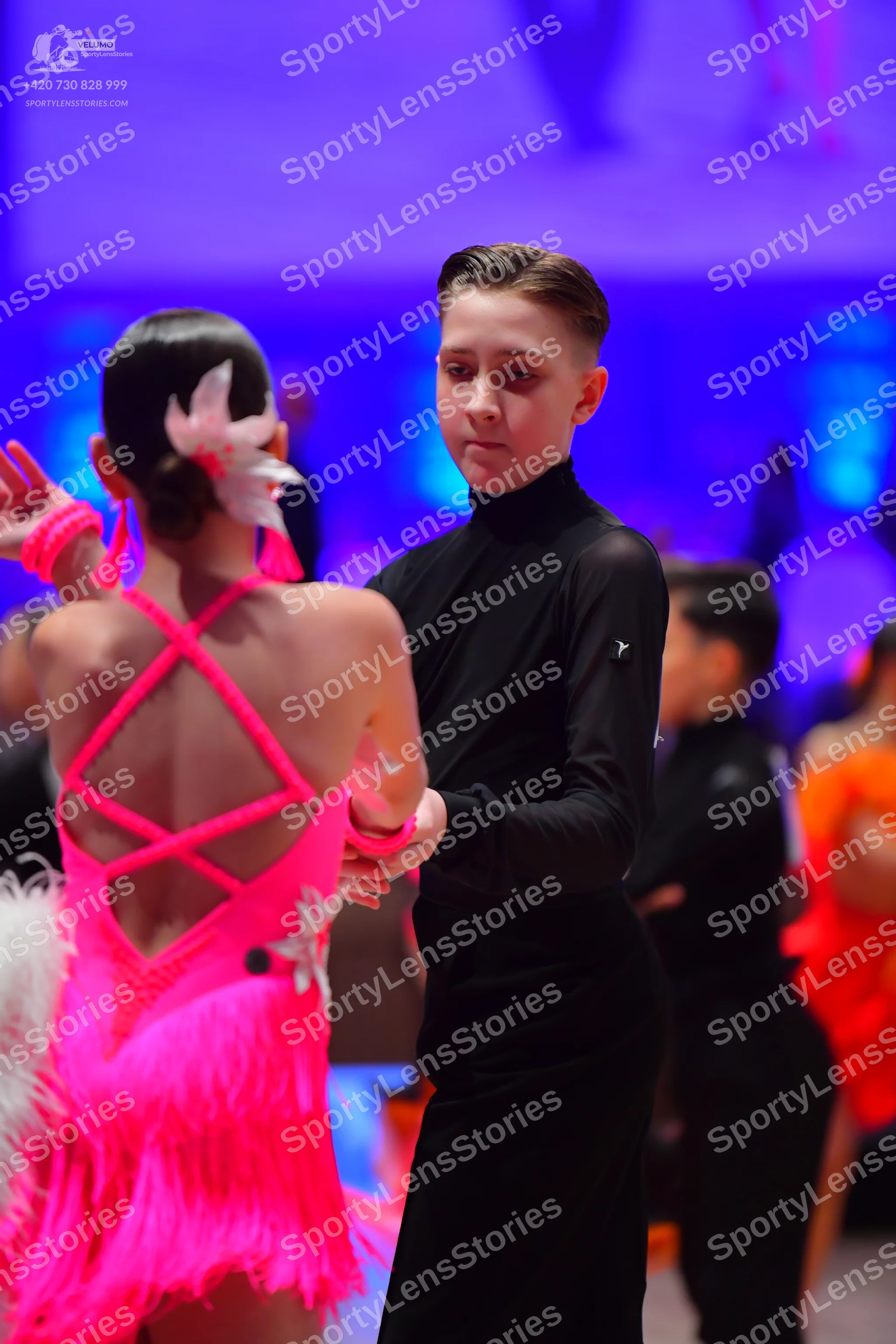 Dancesport competitor: Female dancer in foreground: bright pink Latin dance dress with criss-cross back