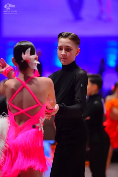 Dancesport competitor: Female dancer in foreground: bright pink Latin dance dress with criss-cross back