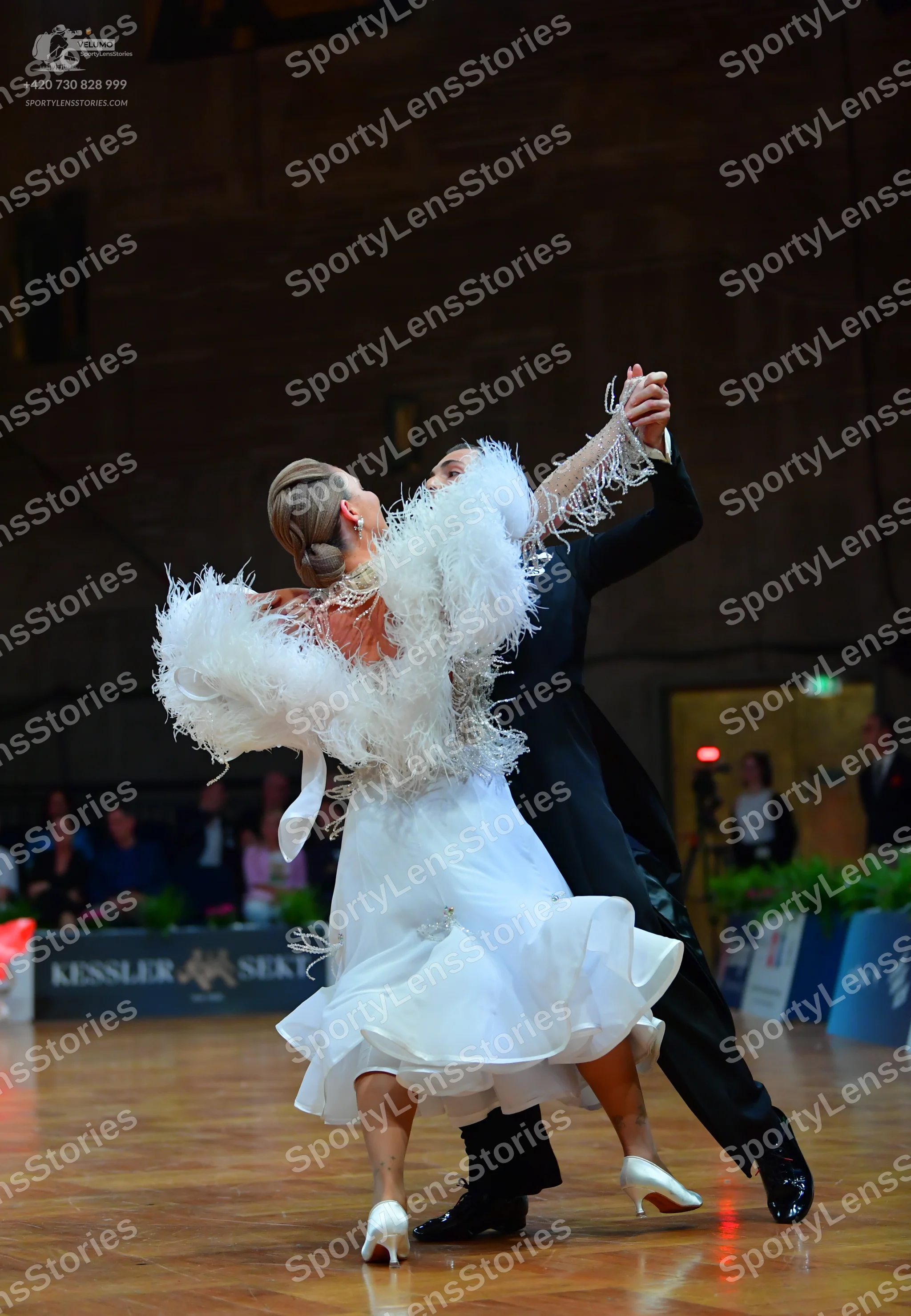 Dancesport competitor: Female dancer: white ballroom dress with large white feather-like trim on the sl