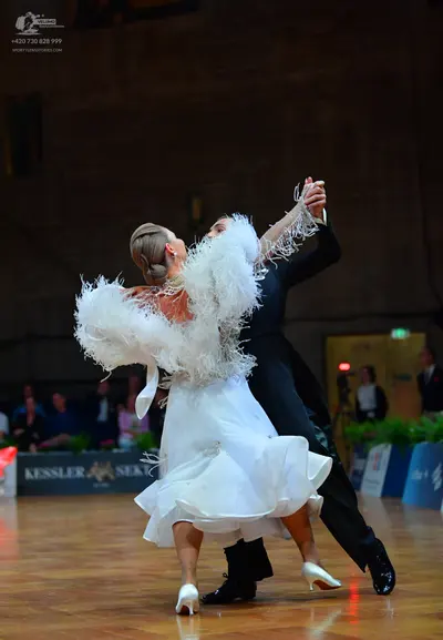 Dancesport competitor: Female dancer: white ballroom dress with large white feather-like trim on the sl
